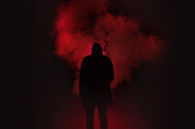 A mysterious silhouette standing against a backdrop of dramatic red smoke.